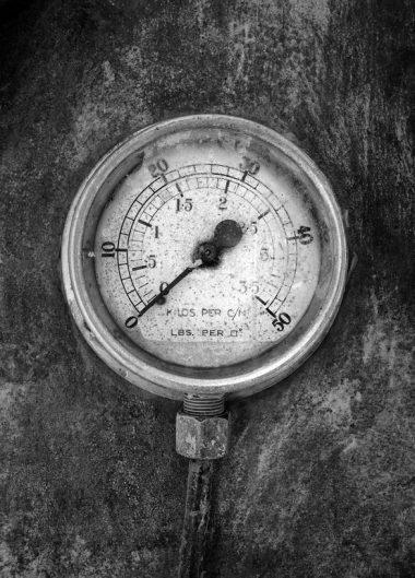 monochrome image of an round industrial pressure gauge with numbers round the dial mounted on a metal surface of a large abandoned diesel powered generator Old air-pressure gauge registering zero pressure - Air compressor equipment leasing | AIRPLUS Industrial